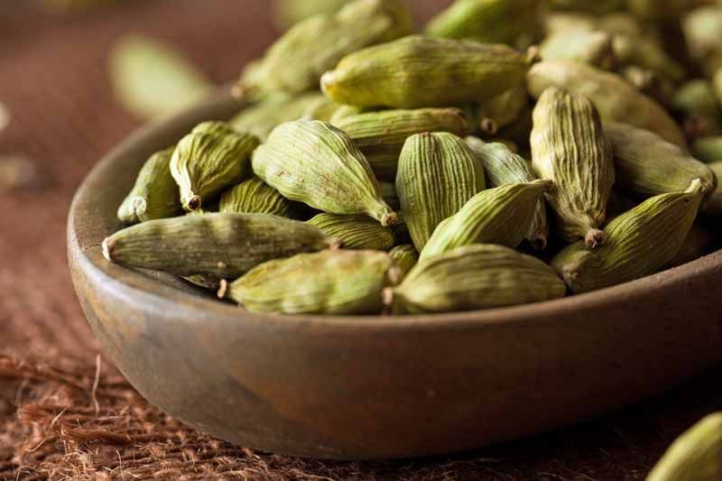 Green cardamom pods in a rustic brown clay bowl, resting on an earthy surface, showcasing the natural texture and color of dried cardamom spice, warm and inviting